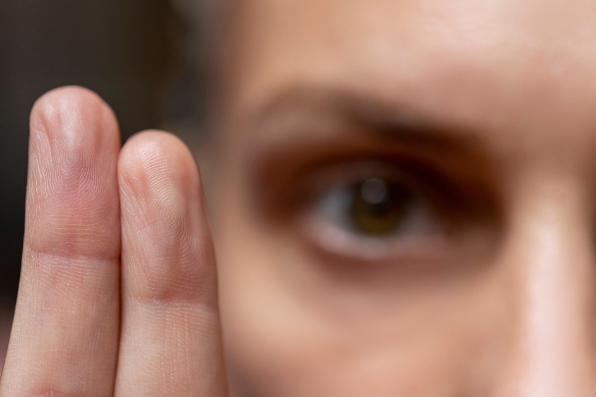 close up of two fingers lifted together and a blurred out eye in the background