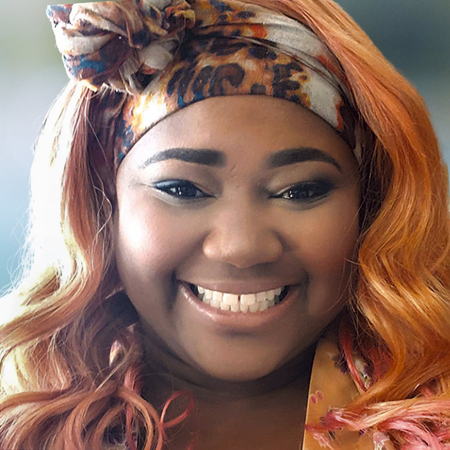 Headshot of Imaria Hardon. A young woman with red hair and bandana smiling.