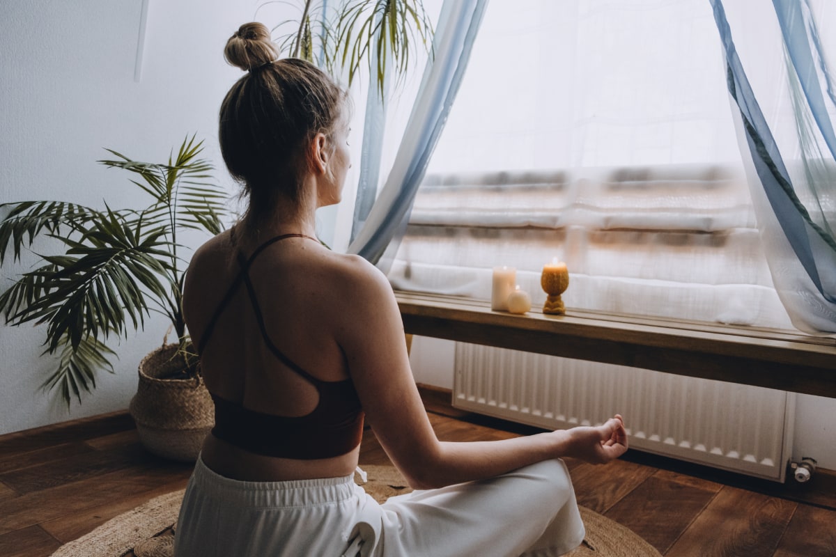 woman in lotus position meditating in front of window with candles on ledge