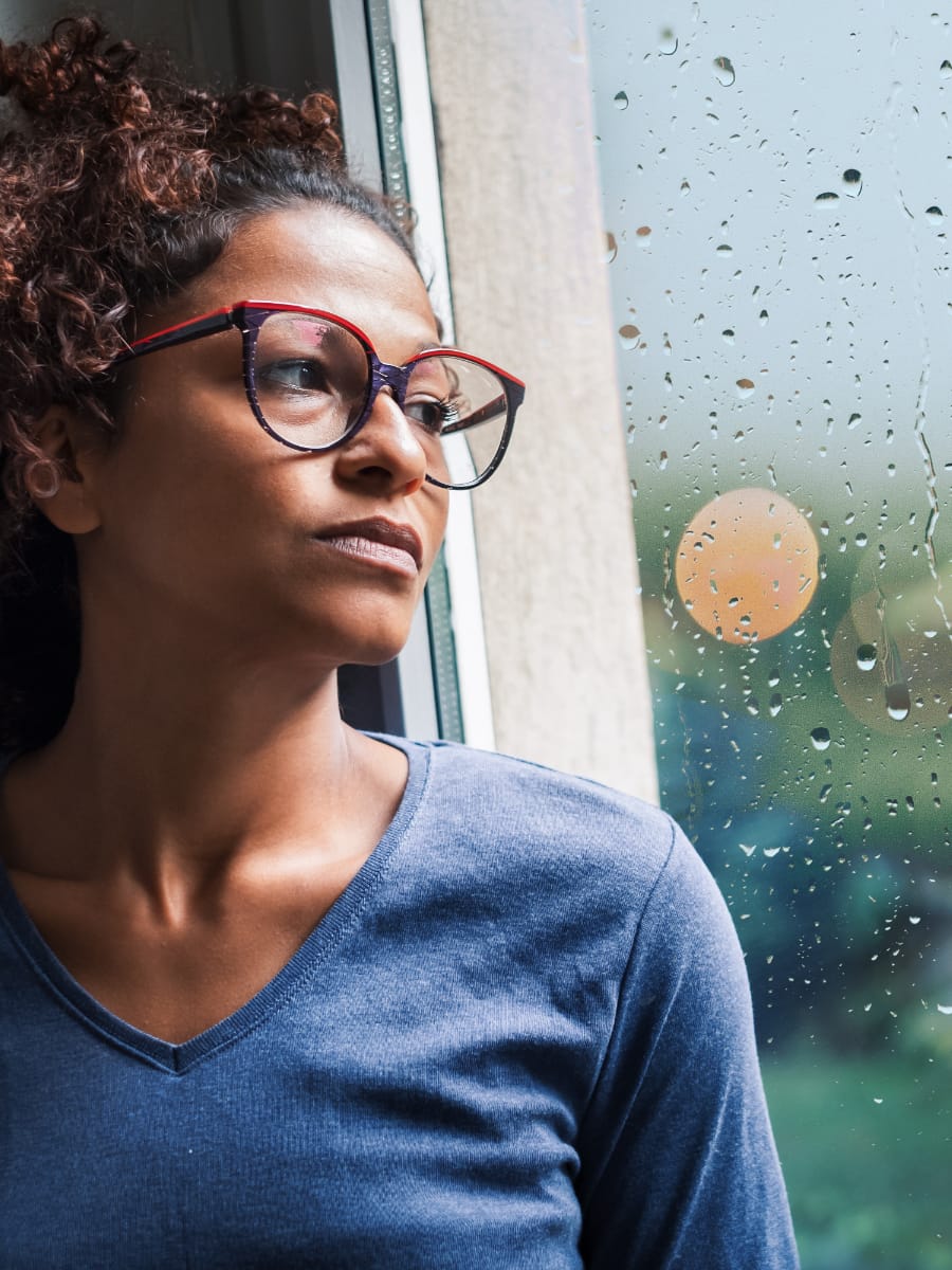 woman with sad look on her face staring out a rainy window