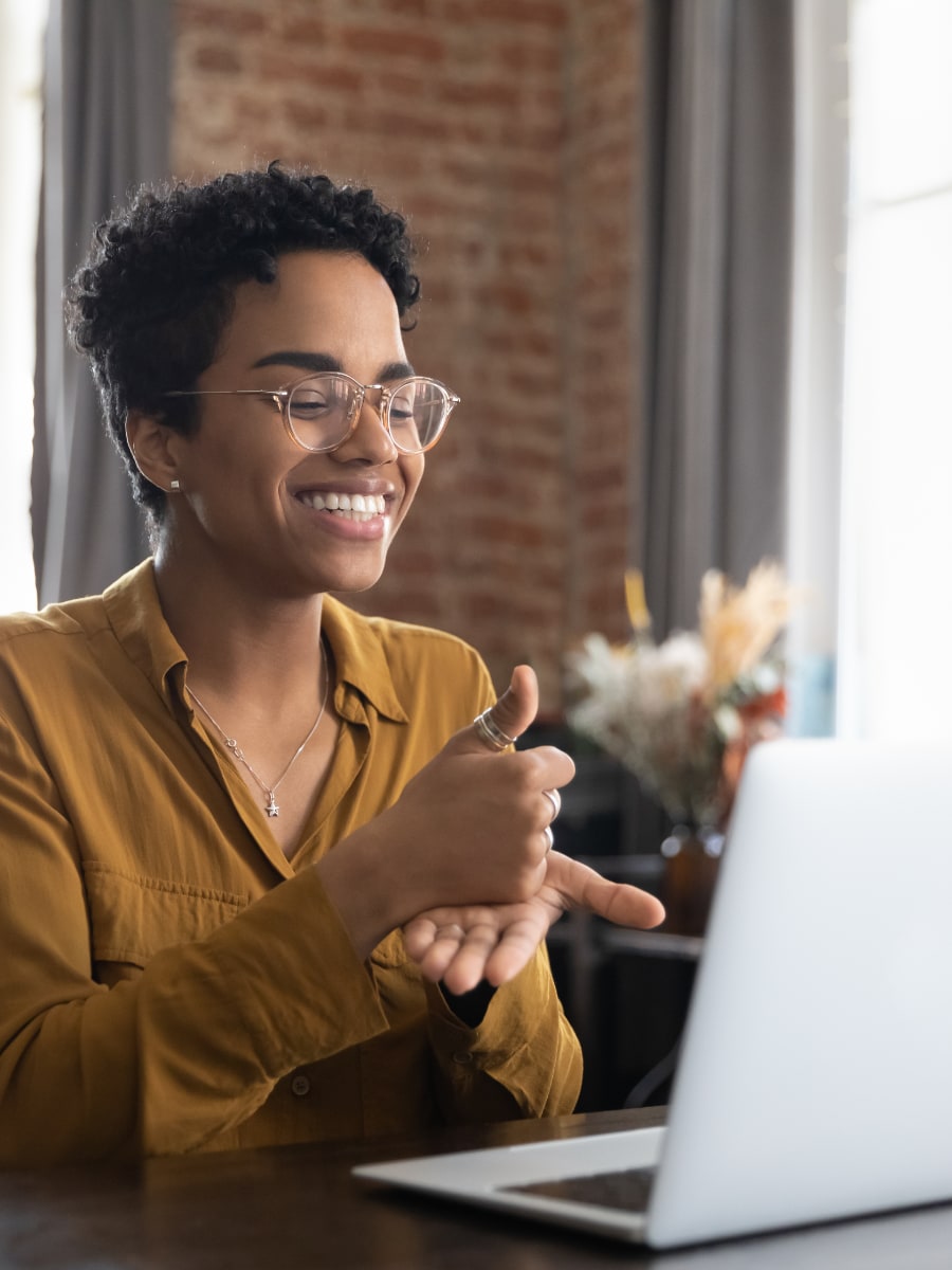smiling woman with short curly hair and glasses looking at laptop and doing sign language