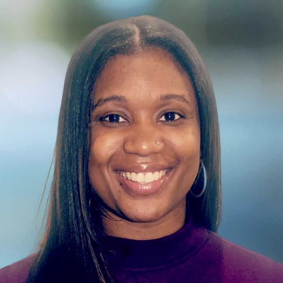 Adayia Davis, therapist, smiles warmly. She has long dark hair and wears a purple top and hoop earrings against a soft blue background.